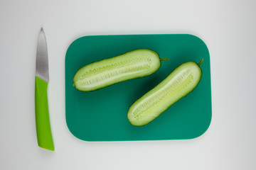 A nice fresh cut cucumber on a chopping Board next to a green knife. Green color in food. For the presentation of a healthy lifestyle.