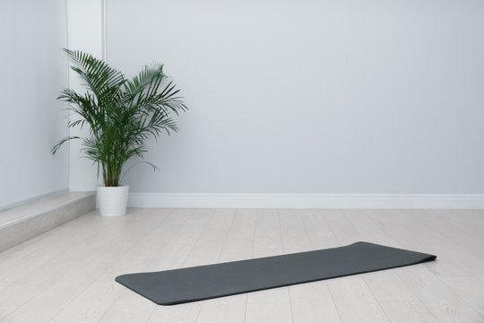 Unrolled Black Yoga Mat On Floor In Room. Space For Text