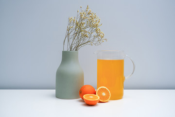 A vase with dried flowers and a glass of orange juice on the white table