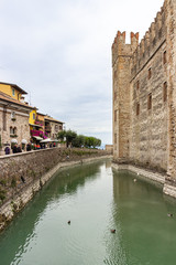 Fototapeta na wymiar Tourists walk along the embankment near the Castello Scaligero fortress wall in the Sirmione town in Lombardy, northern Italy