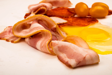 A broken chicken egg without a shell, slices of sausage and bacon and tomatoes on a white background. Close up.