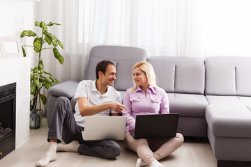 Happy young casual couple sitting working together at home office, smiling.