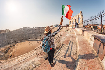 girl holds an Italian flag standing on the steps of an ancient Roman amphitheater. The concept of...