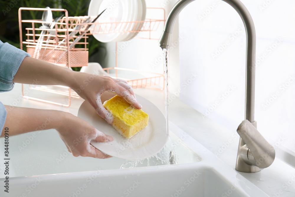 Wall mural Woman washing plate in modern kitchen, closeup