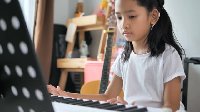Asian little girl learning to play basic piano by using electric synthesizer keyboard for beginner music instrumental self studying at home