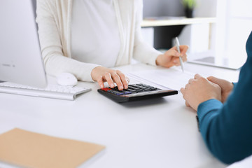 Fototapeta na wymiar Accountant checking financial statement or counting by calculator income for tax form, hands closeup. Business woman sitting and working with colleague at the desk in office toned in blue. Tax and