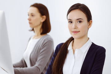 Business woman looking at camera at the background of working colleagues. Office life concept, headshot