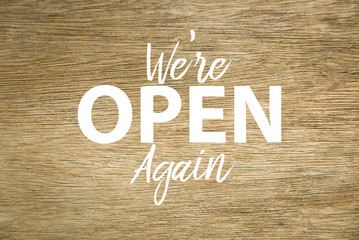 Top view of wooden background written with ' We're Open Again '.