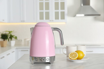 Modern electric kettle, cups and lemons on table in kitchen
