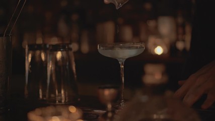 Handheld real time close up shot of a bartender pouring a cocktail into a glass at a bar in Bangkok, Thailand.