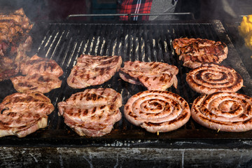 Mixed meat sausages being cooked on a hot black metallic grill in display for sale at a restaurant at a street food market, traditional food photographed with soft focus
