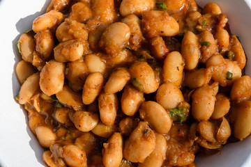 Close up of a large portion of white beans freshly cooked with tomato sauce and hot spices in display at a street food market, healthy vegan food photographed with soft focus
