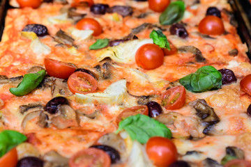 Traditional Italian pizza with fresh tomatoes, artichoke, mushrooms and olives displayed for sale at a street food market festival in Bucharest, Romania, healthy food photographed with soft focus
