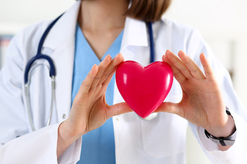Female medicine doctor hands holding and covering red toy heart closeup. Cardio therapeutist, student education, physician make cardiac physical, heart rate measure, arrhythmia concept
