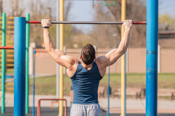 Fototapeta premium Young strong guy pulls himself up on the horizontal bar.