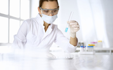 Female laboratory assistant analyzing test tube with blue liquid. Medicine, health care and researching concept