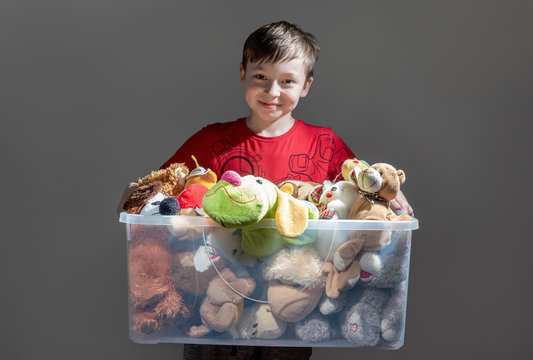 Boy holding a toys in box on dark background. Donatation. Copy space for text