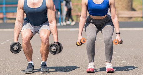 Athletic guy and girl lunges with dumbbells at the playground. Health care.