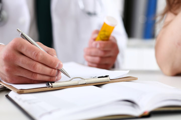 Male medicine doctor hand hold jar of pills and write prescription to patient at worktable. Panacea and life save, prescribing treatment, legal drug store concept. Empty form ready to be used
