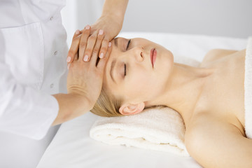 Fototapeta na wymiar Beautiful caucasian woman enjoying facial massage with closed eyes in spa salon. Relaxing treatment in medicine and Beauty concept