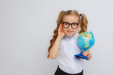 a little girl in a school uniform and glasses eavesdropping holds a globe in her hands on a white...