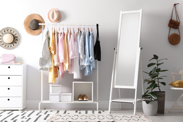 Rack with stylish women's clothes and mirror indoors. Interior design