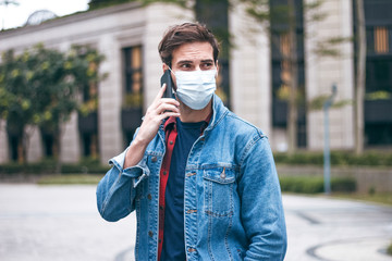 Obraz premium A mature handsome man with a beard talking on his mobile phone and wears a face pollution mask to protect himself from coronavirus on the street.