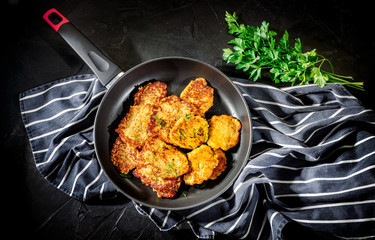 Potato pancakes with sour cream, herbs, garlic and spices on a dark background