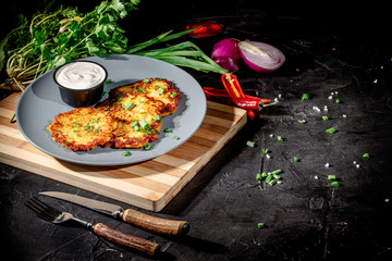 Potato pancakes with sour cream, herbs, garlic and spices on a dark background