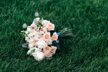 Obraz na płótnie Canvas Wedding bouquet with white pink yellow roses and greenery eucalyptus on a background of grass with a blue ribbon decor