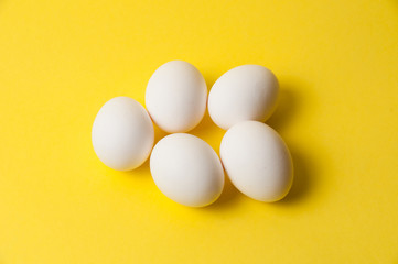 Several chicken eggs on a bright yellow background, copy space