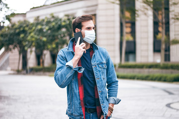 A mature handsome man with a beard talking on his mobile phone and wears a face pollution mask to protect himself from coronavirus on the street.