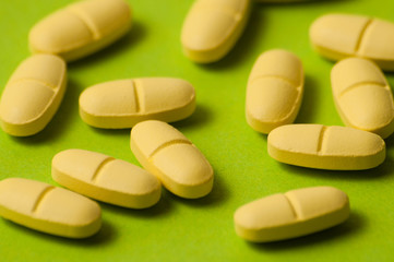 Many pills, antibiotics or vitamins yellow color on a green background close-up, close-up