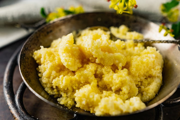 Hot corn porridge with sugar and butter on an old rustic pan and a metal vintage stand. Next to it is a sprig of flowering black currant with yellow flowers