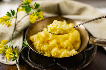 Hot corn porridge with sugar and butter on an old rustic pan and a metal vintage stand. Next to it is a sprig of flowering black currant with yellow flowers