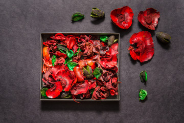 Carton box with red potpourri flowers and leaves on black background, top view, mockup