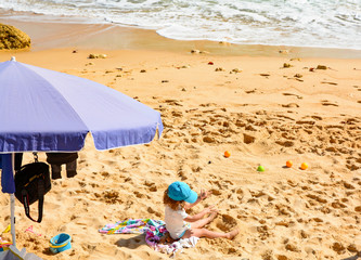 Sandy beach, baby under an umbrella playing in the sand.