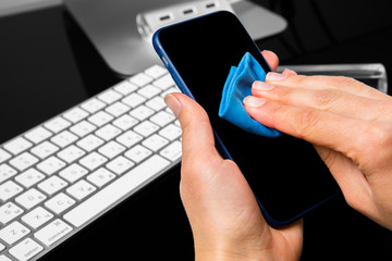 Woman Wiping Mobile Phone Screen With Sanitizer on wood background. Cleaning smart phone screen to prevent corona virus Covid 19