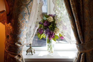A bouquet of purple and white lilac in a glass vase on a windowsill.
