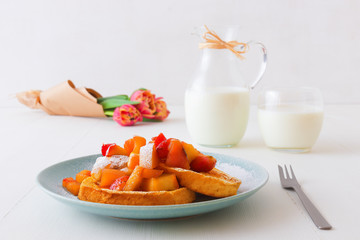 French toast with stewed apples and strawberries, with cup of coffee and tulip flowers served on white wooden table. French toast or also pain perdu or last loaf or eggy bread.