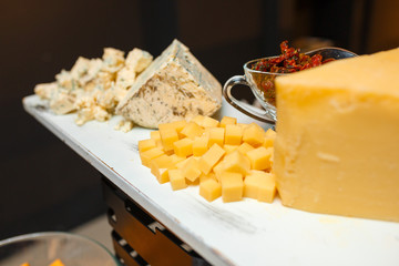 Assorted cheeses on a white board on a dark background.