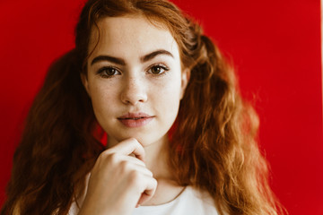 bright red-haired girl with expressive eyes propped her chin on a red background