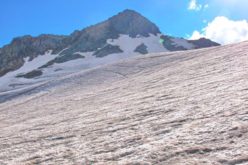 Not melted snow on top of the mountain, in the background of the mountain covered with snow, shining bright sun.