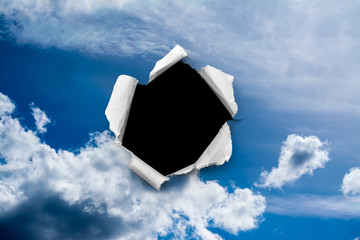 A hole in the day sky with torn edges, as on paper, with an isolated black copyspace background in...