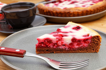 Piece of homemade raspberry pie with yogurt filling and cup of tea on wooden table. Shallow focus.