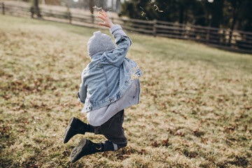Little boy in a denim jacket and hat plays with autumn leaves in a forest glade in the mountains.