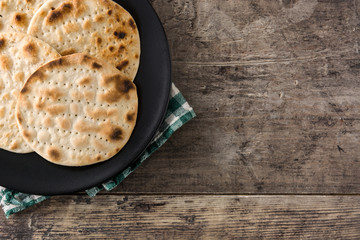 Handmade matzah for Jewish Passover in black plate on wooden table. Top view. Copy space