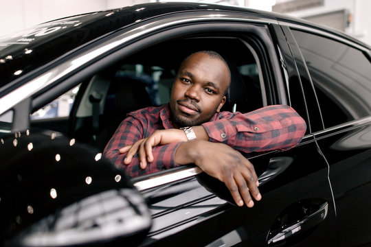 African Man Sitting Behind The Wheel Of A New Black Business Class Car Looking Out Of The Window