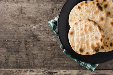 Handmade matzah for Jewish Passover in black plate on wooden table. Top view. Copy space