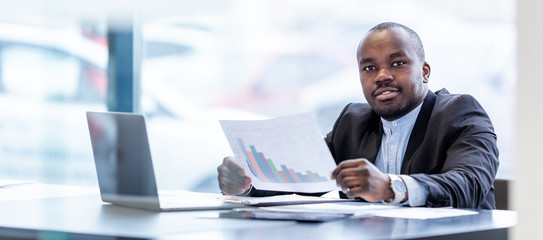 African businessman sitting at the Desk in the office, looking at the currency quotes on the chart